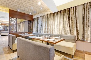 A restaurant with booth seating, tables set for dining, and a patterned curtain backdrop. - Townhouse OAK Hotel Berrys (Bangalore)