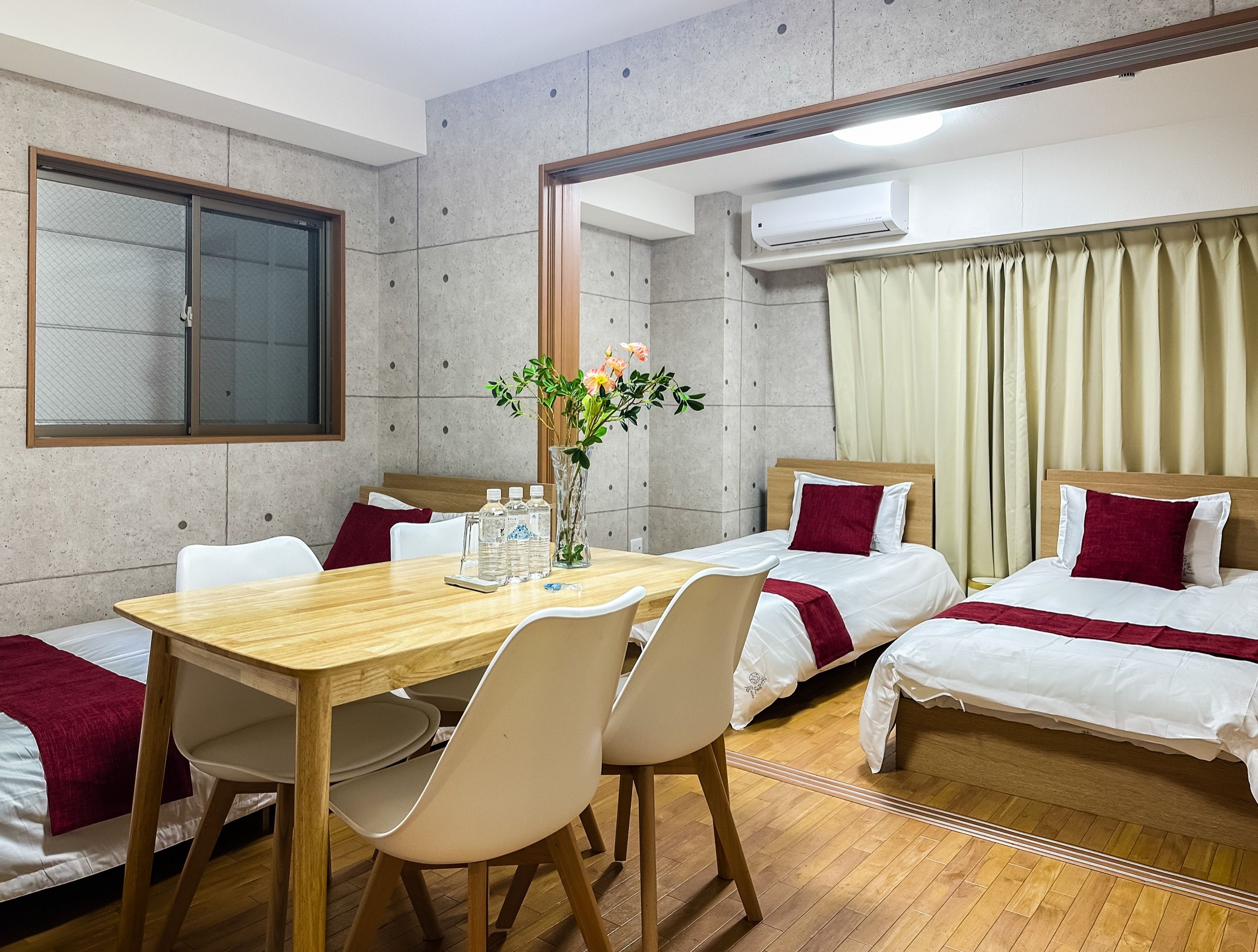 A hotel room with a wooden dining table, two single beds, a large mirror, and an air conditioning unit.