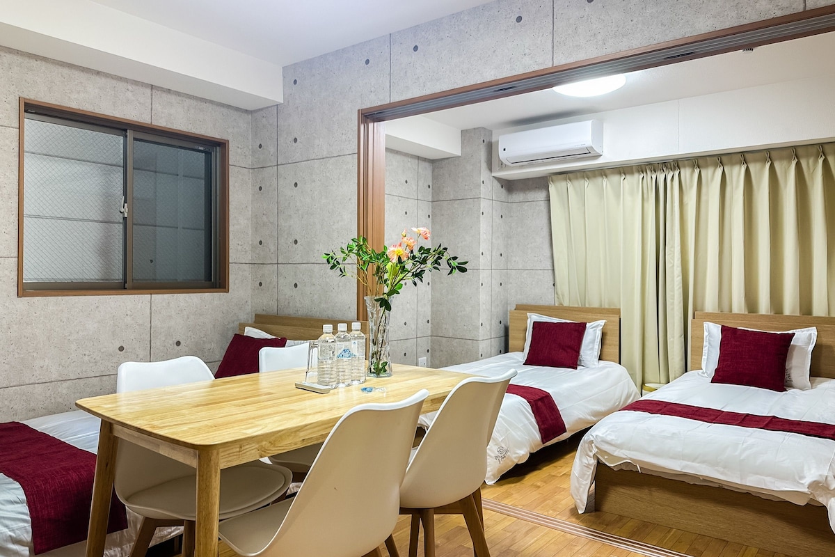 A hotel room with a wooden dining table, two single beds, a large mirror, and an air conditioning unit.