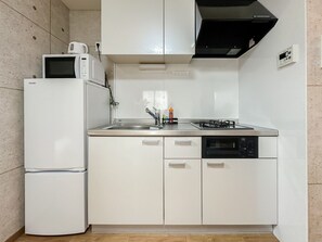 Een kleine keuken, voorzien van een koelkast, magnetron, spoelbak, kookplaat en vaatwasser.