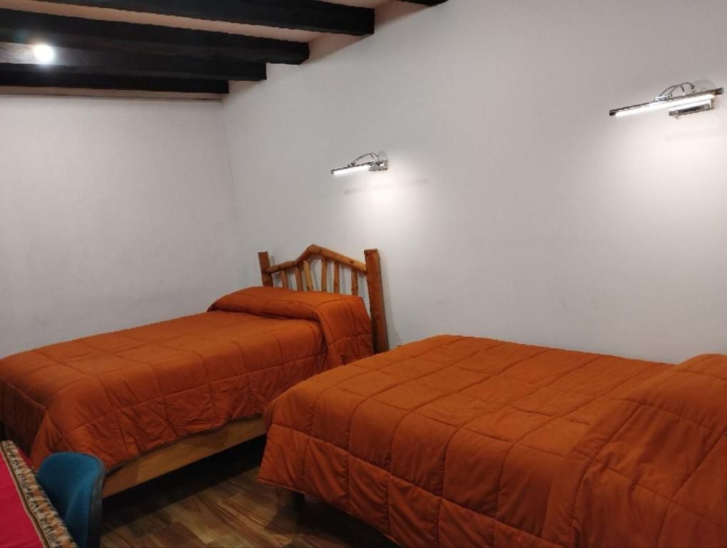 Een kamer met twee eenpersoonsbedden, houten hoofdeinden en een zithoekje met een stoel.