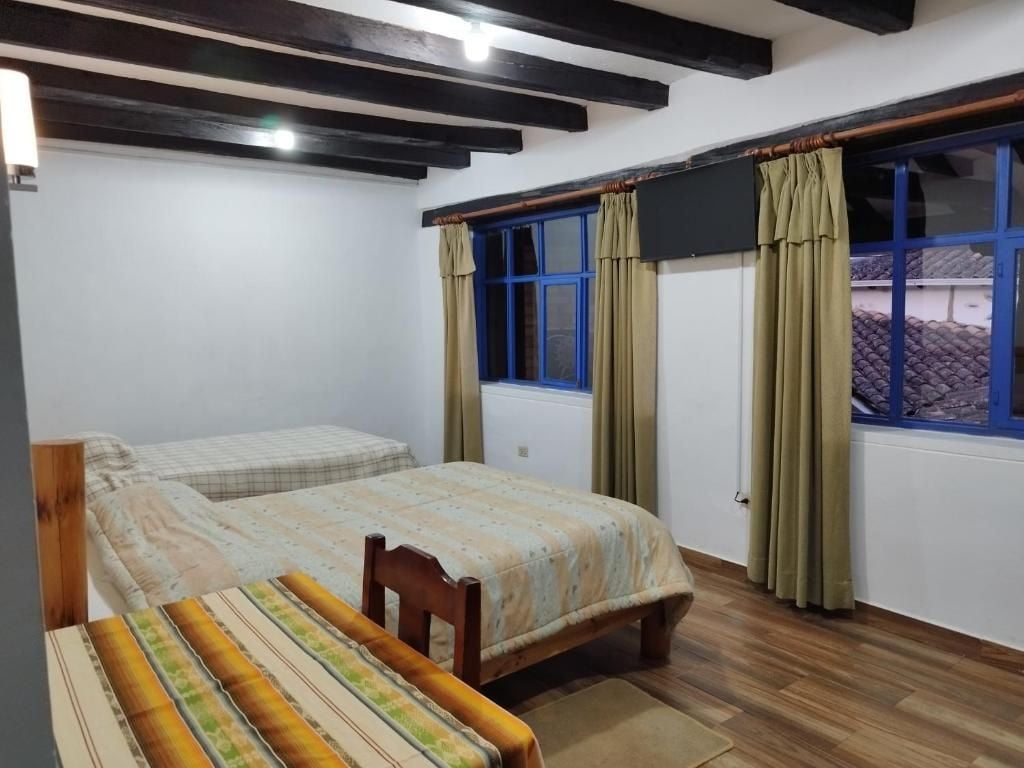 A room with two beds, a wooden bench, a window with curtains, and a blackboard on the wall.