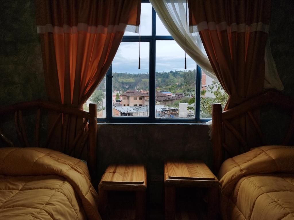 A room with two beds, a window with curtains, and a view of buildings outside.