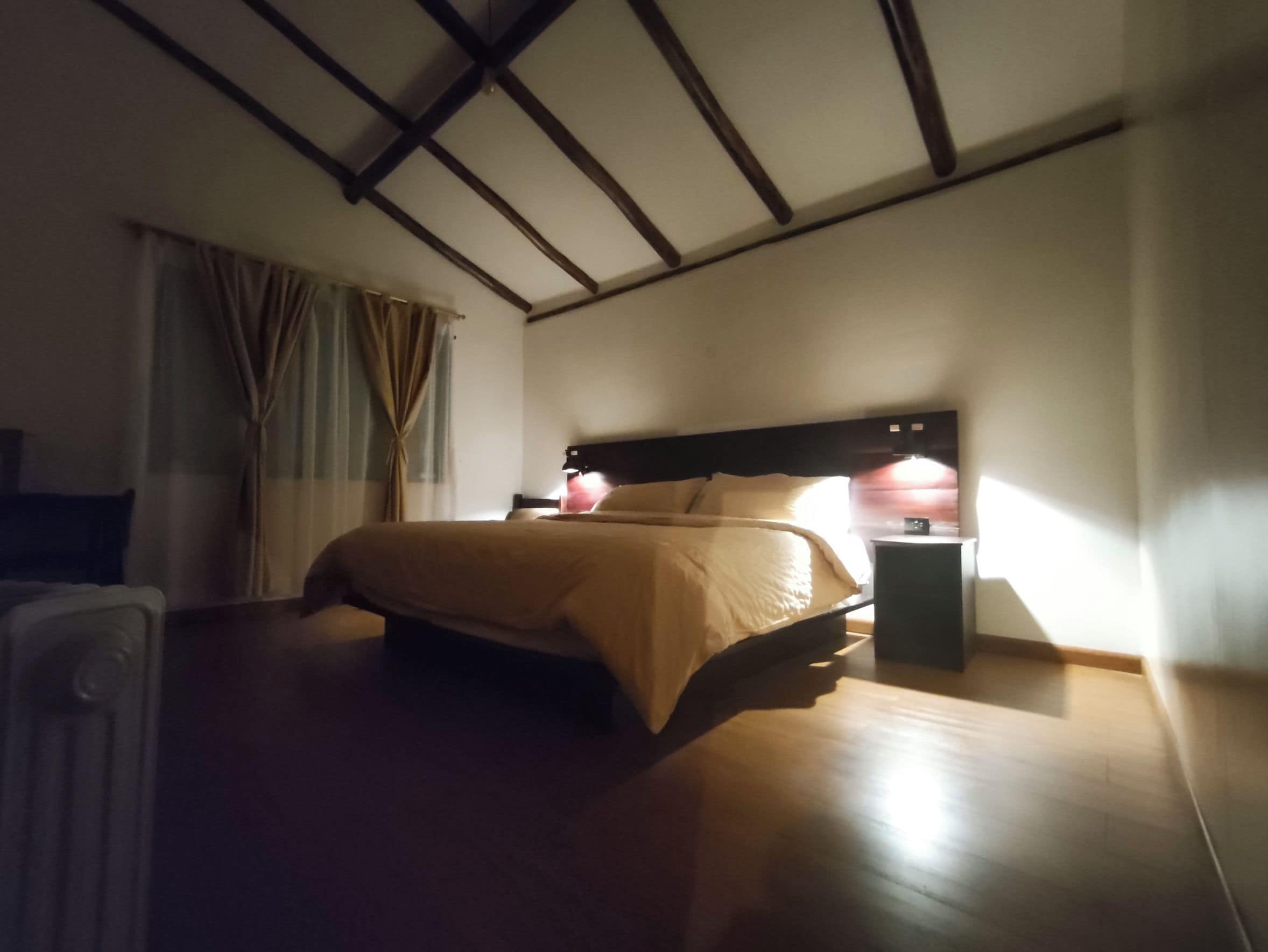 Habitación de hotel con cama, mesita de noche y ventana con cortinas.