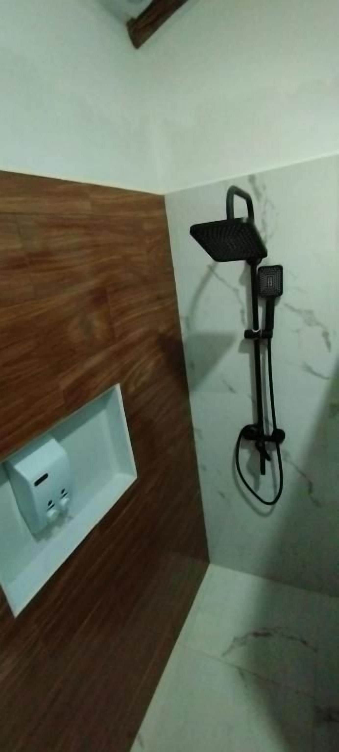 Un baño con tocador de madera, un lavabo blanco con toma de corriente y un cabezal de ducha manual negro montado en la pared.