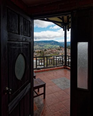 A wooden door leading to a balcony with a view of a town and mountains. - Achik Wasi (Saraguro)