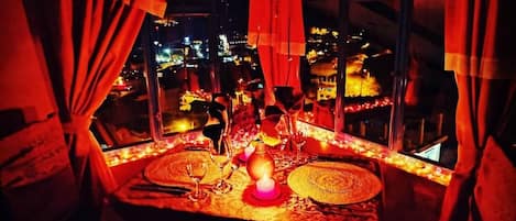 A table set with a candle, glasses, and a decorative centerpiece, overlooking a cityscape at night.