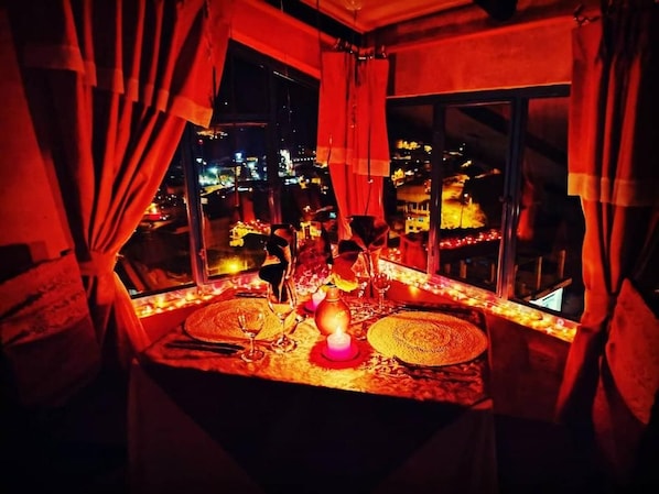 A table set with a candle, glasses, and a decorative centerpiece, overlooking a cityscape at night.