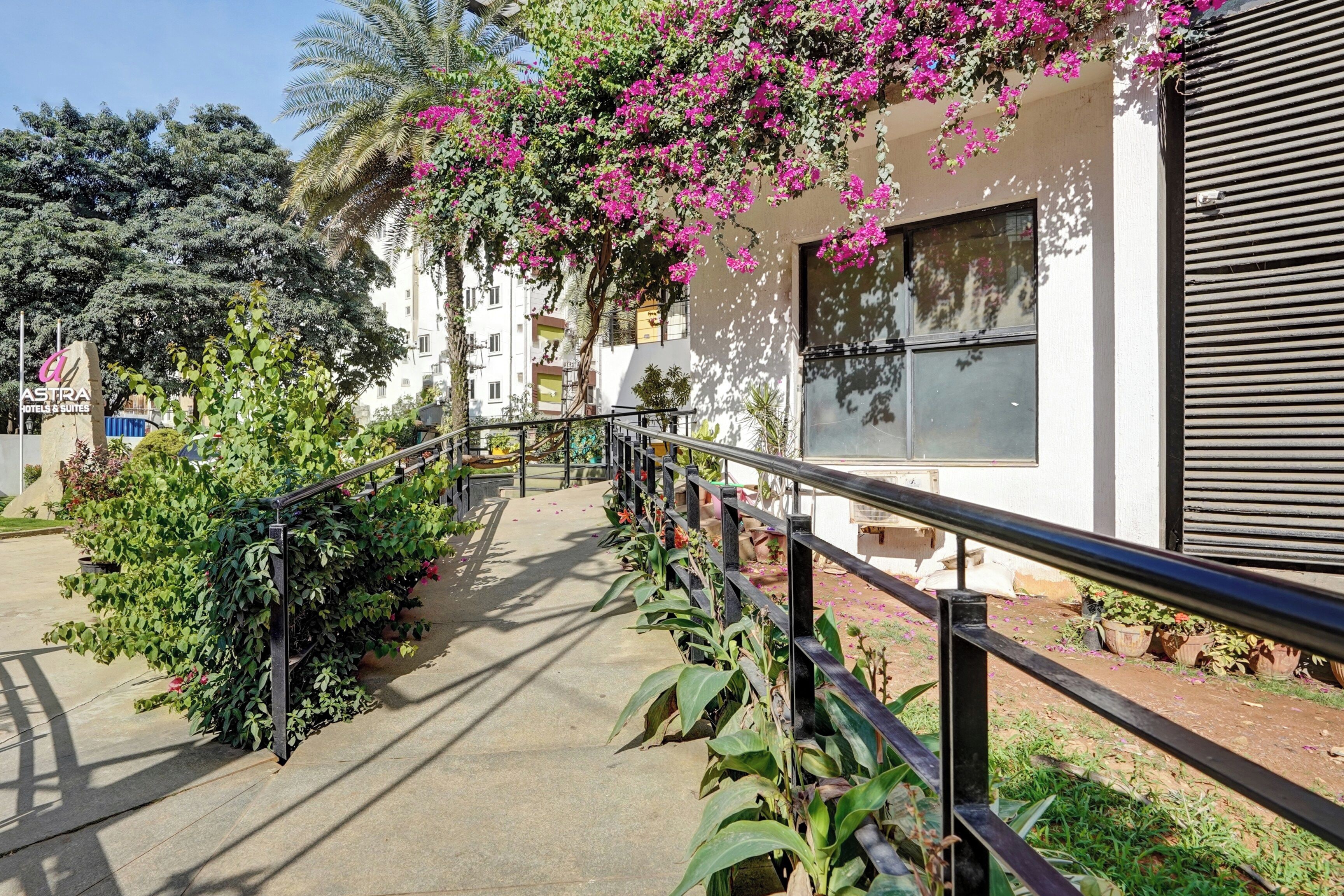 A pathway leading to a building with a balcony adorned with pink flowers.