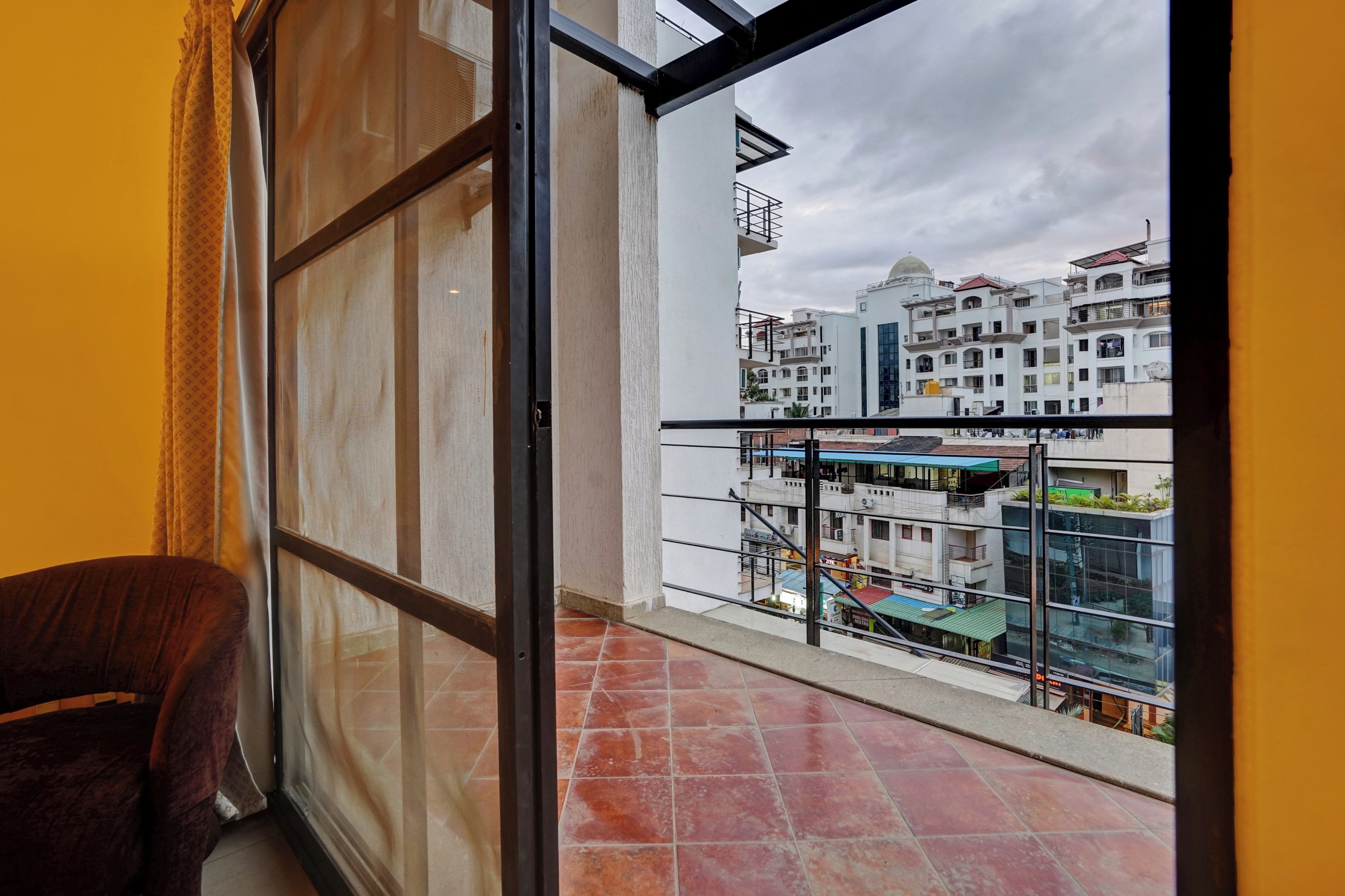 Un balcón con vistas a un paisaje urbano, una silla y una ventana con cortinas.