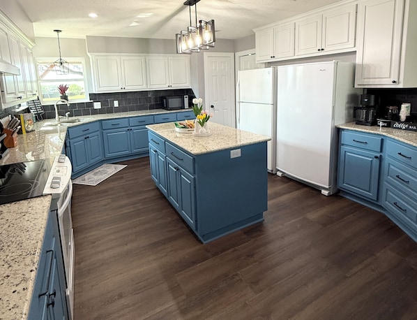 A modern kitchen with blue cabinets, a central island, and a stainless steel refrigerator.