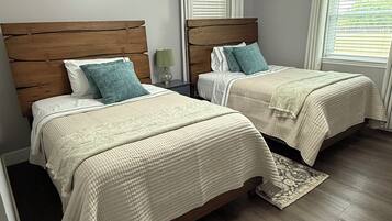 A bedroom with two beds, wooden headboards, white bedding, and a window with blinds.