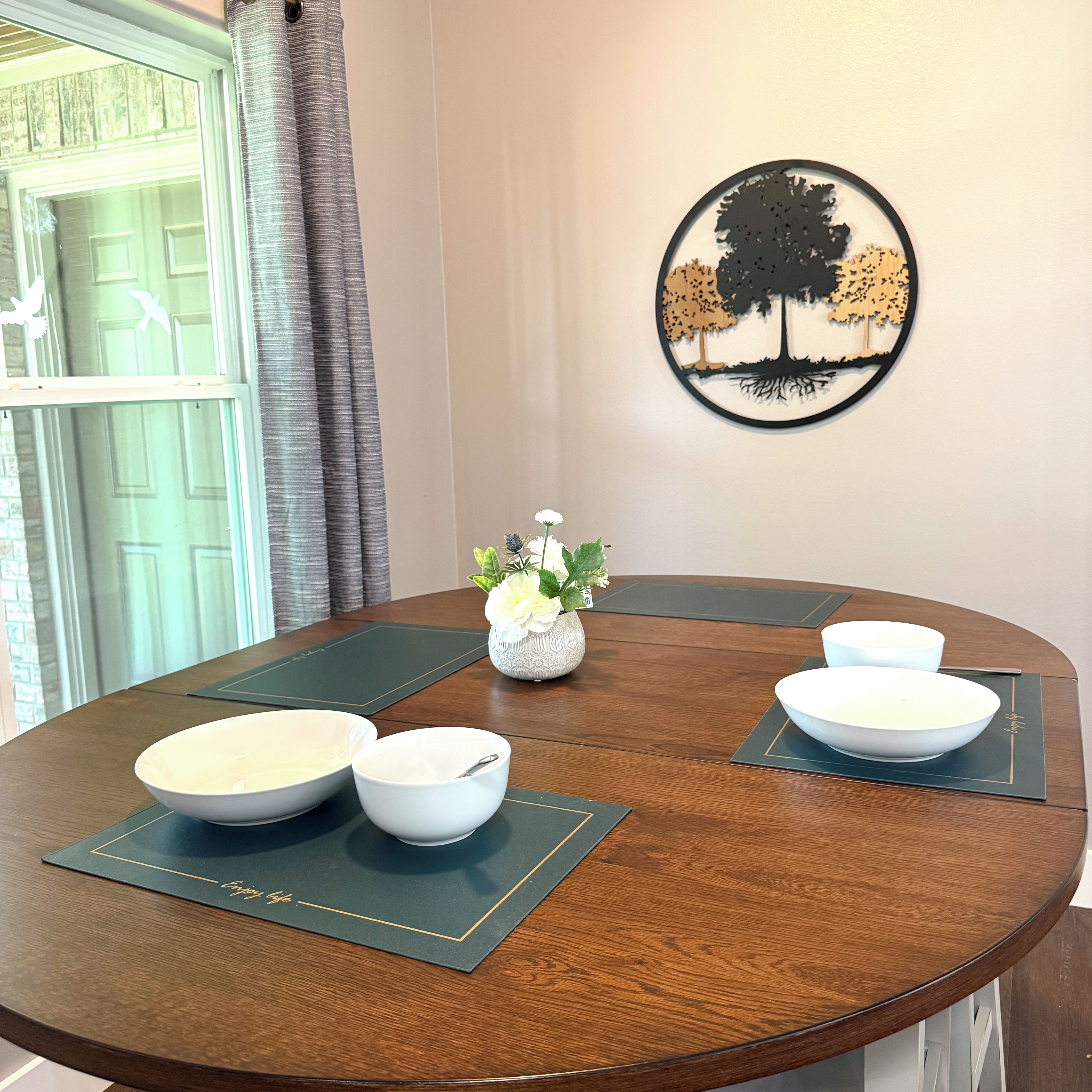 A round dining table with four white bowls and a vase with white flowers.