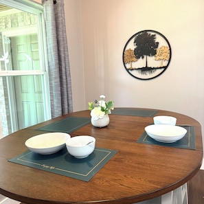 A round dining table with four white bowls and a vase with white flowers.