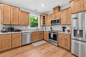 A modern kitchen with wooden cabinets, stainless steel appliances, and a granite countertop. - Asheville Retreat | Hot Tub • Game Loft • Views! (Asheville)