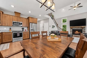 A modern kitchen with wooden cabinets, stainless steel appliances, and a dining area with a wooden table and chairs. - Asheville Retreat | Hot Tub • Game Loft • Views! (Asheville)