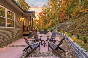 A patio with Adirondack chairs, a fire pit, and a stone wall. - Asheville Retreat | Hot Tub • Game Loft • Views! (Asheville)