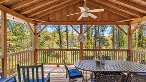 A covered outdoor area with a table and chairs, a ceiling fan, and a view of trees and sky. - The Water Lily | Charming Waterfront Retreat | 4BR (Hendersonville)
