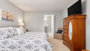 A bedroom with a bed, dresser, chair, and a television. - The Water Lily | Charming Waterfront Retreat | 4BR (Hendersonville)