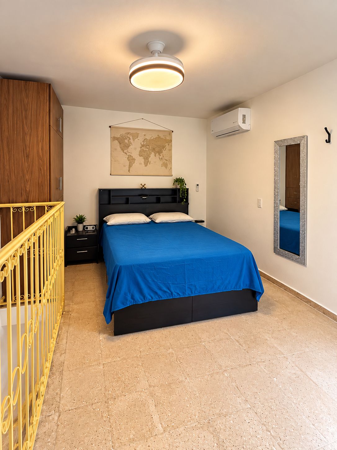 Une chambre à coucher avec un lit, une carte accrochée au mur, un miroir et un escalier.