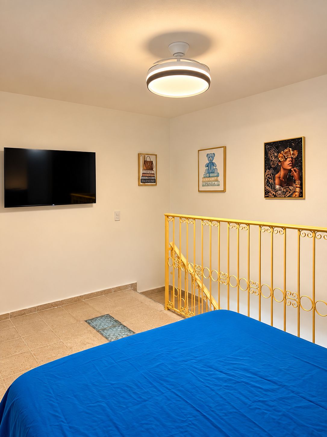 A bedroom with a bed, a television mounted on the wall, and a staircase with a railing.