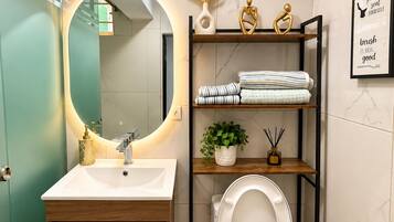Une salle de bain moderne avec un meuble-lavabo, des toilettes et une étagère où sont rangées des serviettes et des objets décoratifs.
