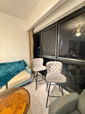 A modern living room with a sofa, two chairs, a coffee table, and a large window with a city view. - Wake up to stunning KL skyline views in this bright 2-bedroom in Bukit Bintang.. (Kuala Lumpur)