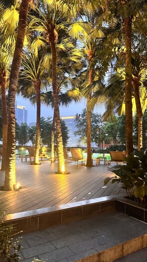 An outdoor area with palm trees and a wooden deck. - Wake up to stunning KL skyline views in this bright 2-bedroom in Bukit Bintang.. (Kuala Lumpur)