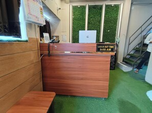 En reception med et skilt, der angiver udtjekningstid kl. 9:00, en trædisk, en telefon og en grøn væg med lodrette paneler.