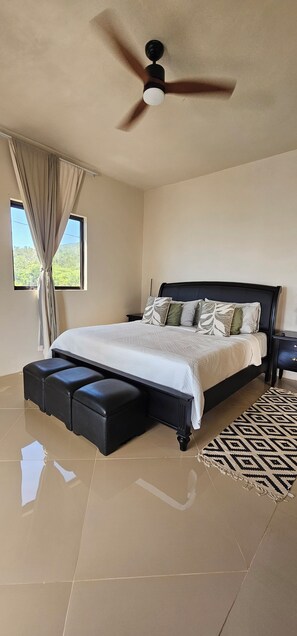 Une chambre à coucher avec un lit, un ventilateur de plafond, une fenêtre avec des rideaux et un tapis à motifs.