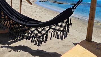 Une scène de plage avec un hamac sous une structure en bois, une table et une vue sur l’océan.
