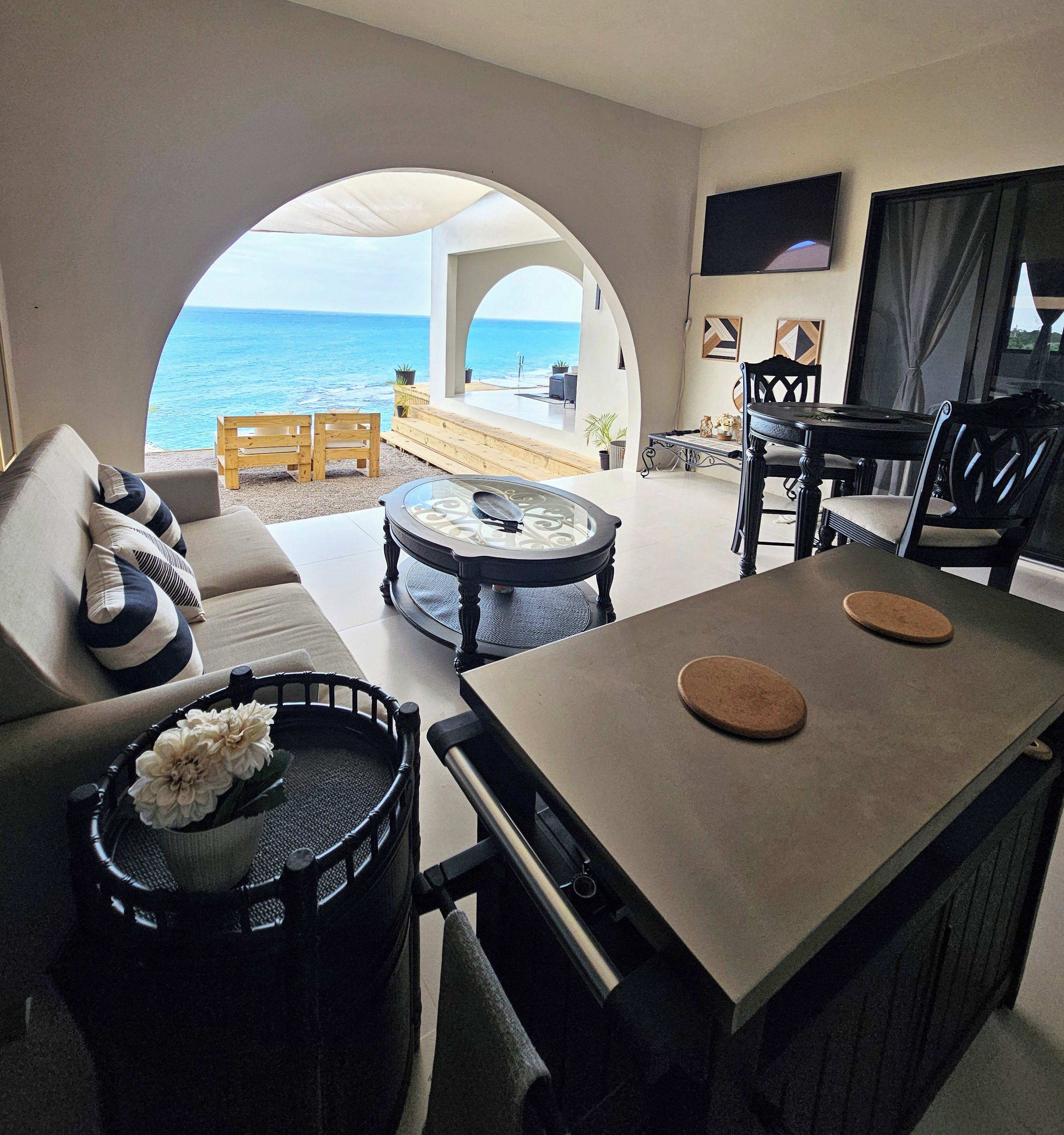 Un salon moderne avec vue sur la mer, comprenant un canapé, une table basse et un coin repas avec des chaises.