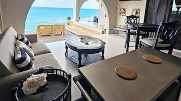 Un salon moderne avec vue sur la mer, comprenant un canapé, une table basse et un coin repas avec des chaises.