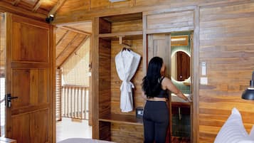 A wooden cabin interior with a bed, a robe hanging on a rack, and a bathroom with a mirror.