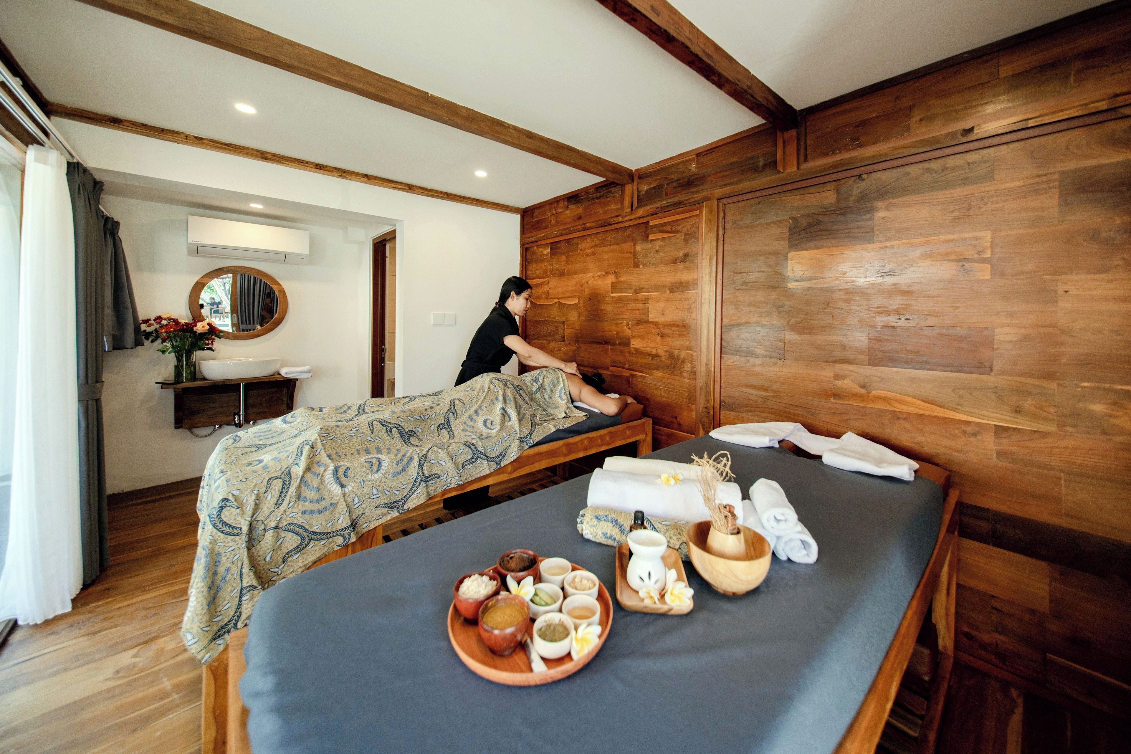 A room with a bed, a wooden wall, a mirror, and a small table with towels and toiletries.
