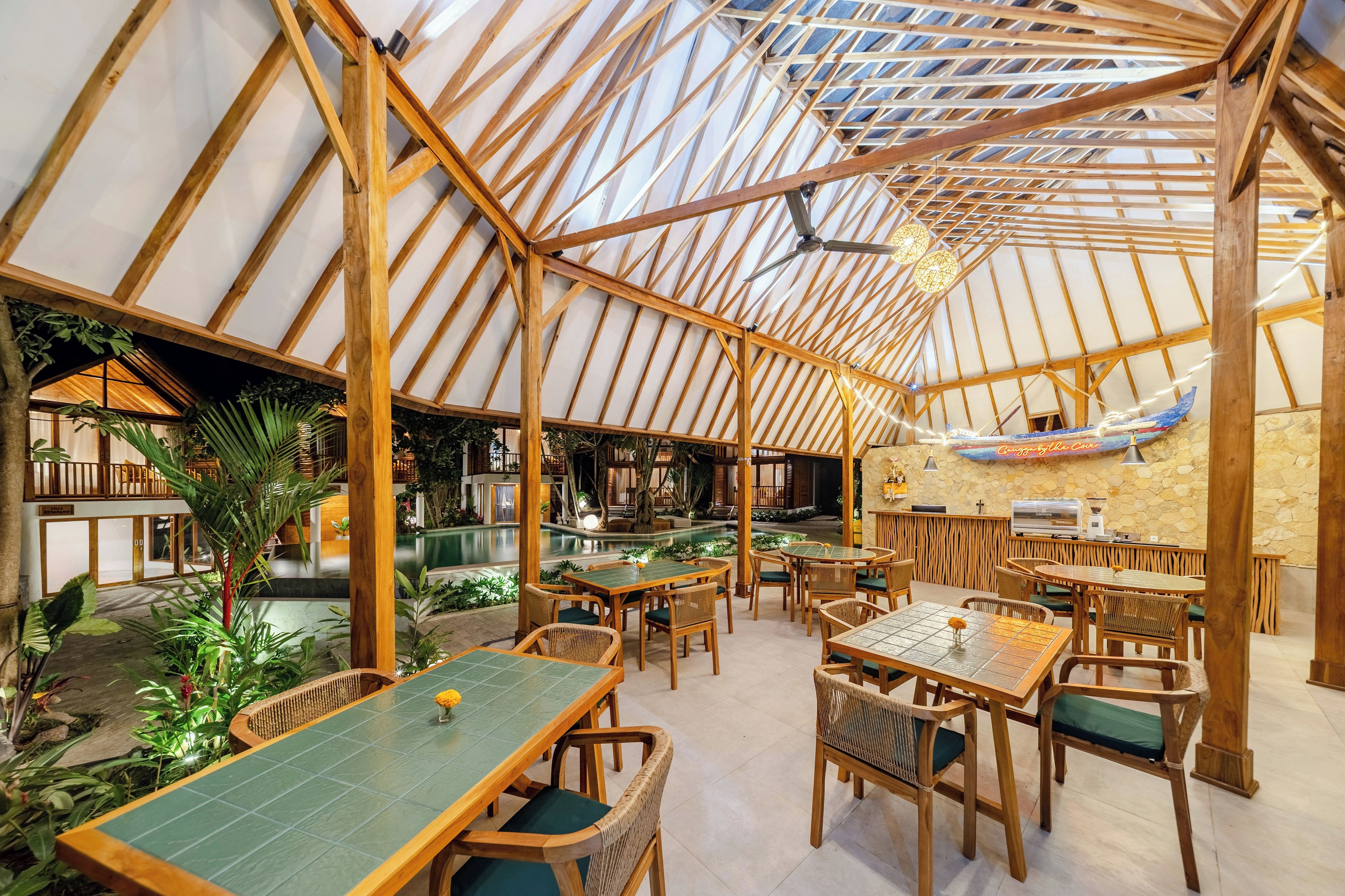 A restaurant with a high wooden ceiling and tables with green cushions.