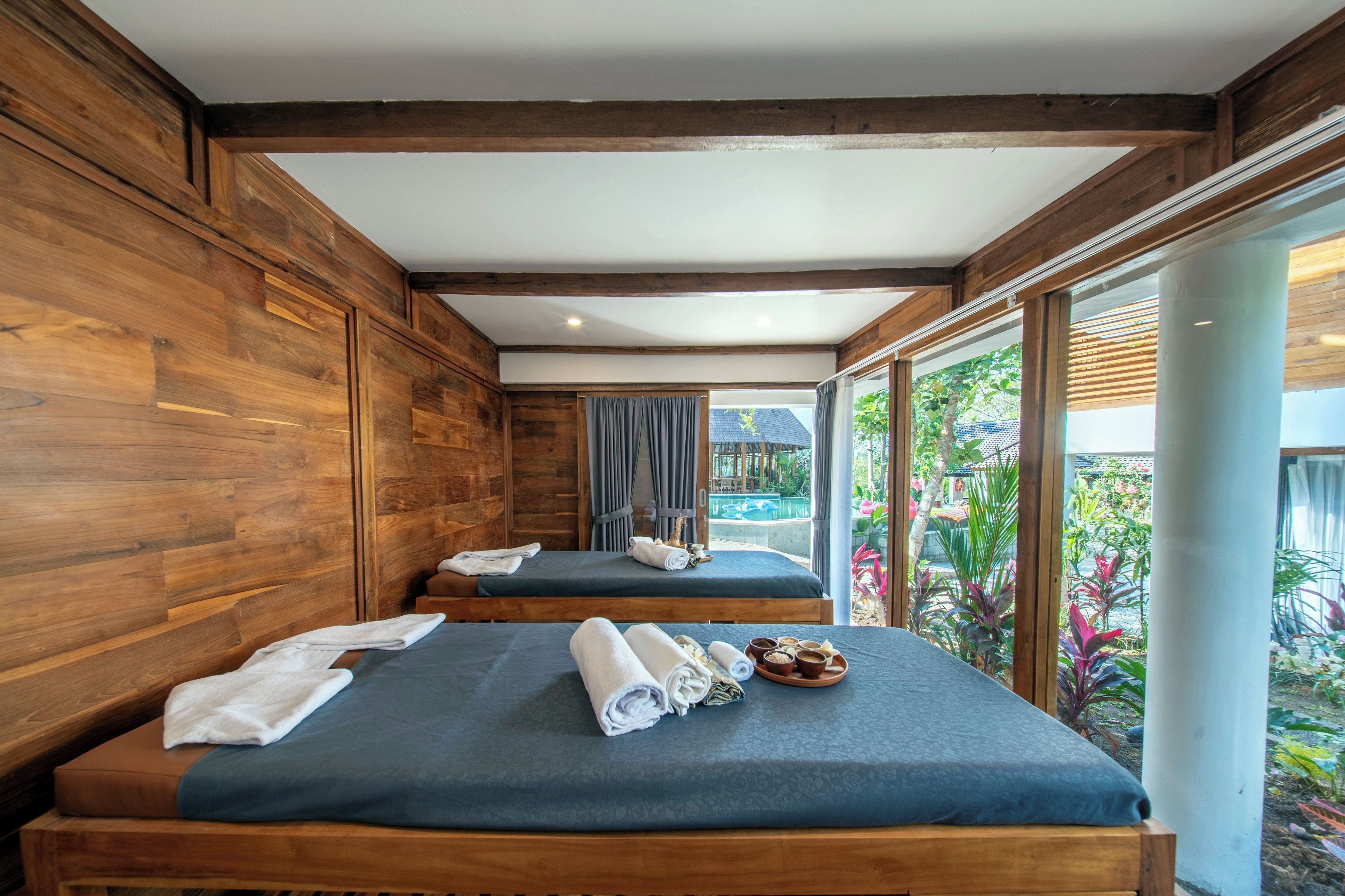 Habitación de hotel con dos camas, paredes de madera, un ventanal grande y vistas a un jardín.