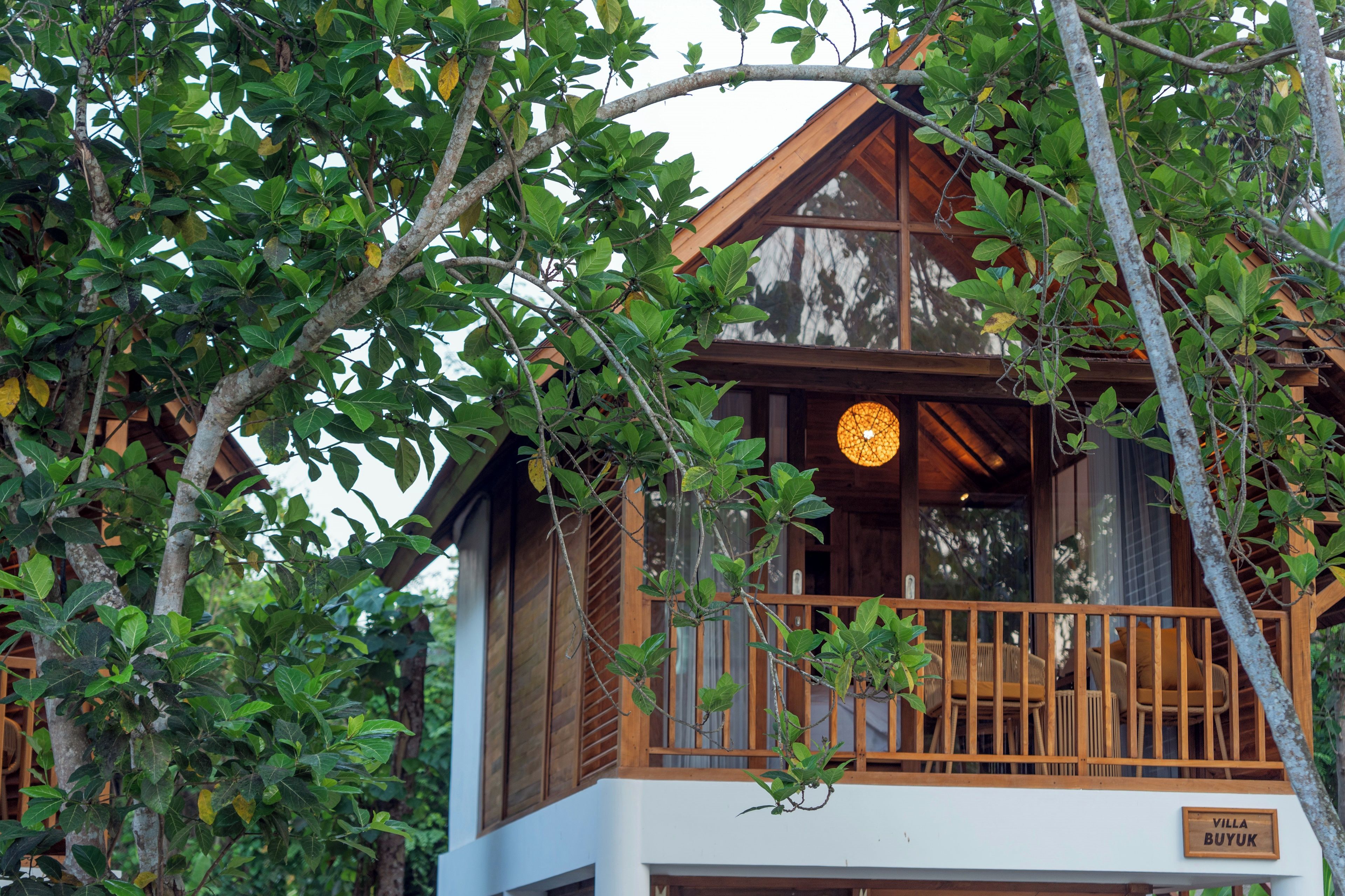 A wooden villa with a balcony, surrounded by lush greenery.