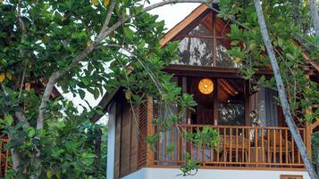 A wooden villa with a balcony, surrounded by lush greenery.