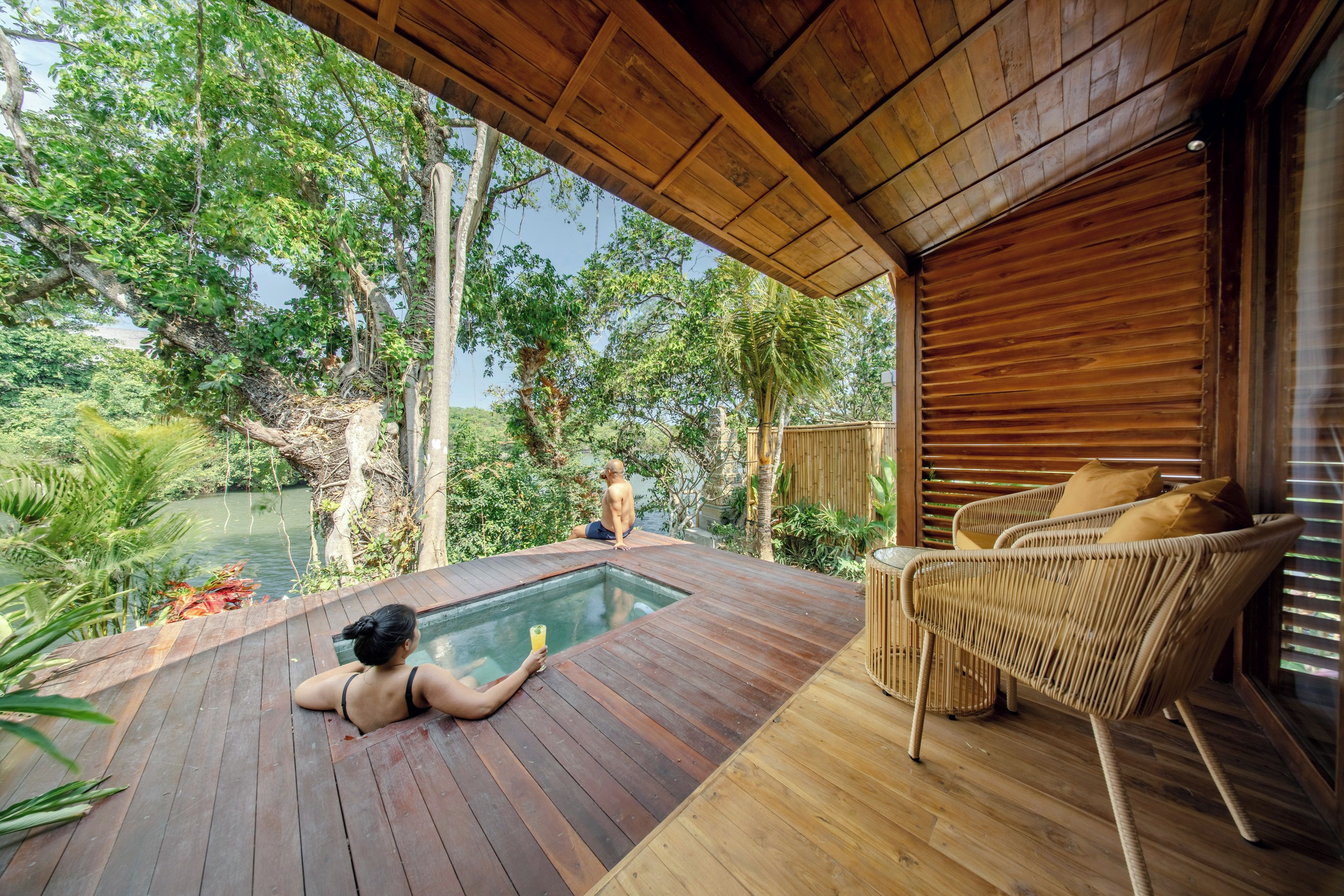 Una terraza de madera con piscina, rodeada de exuberante vegetación y árboles.