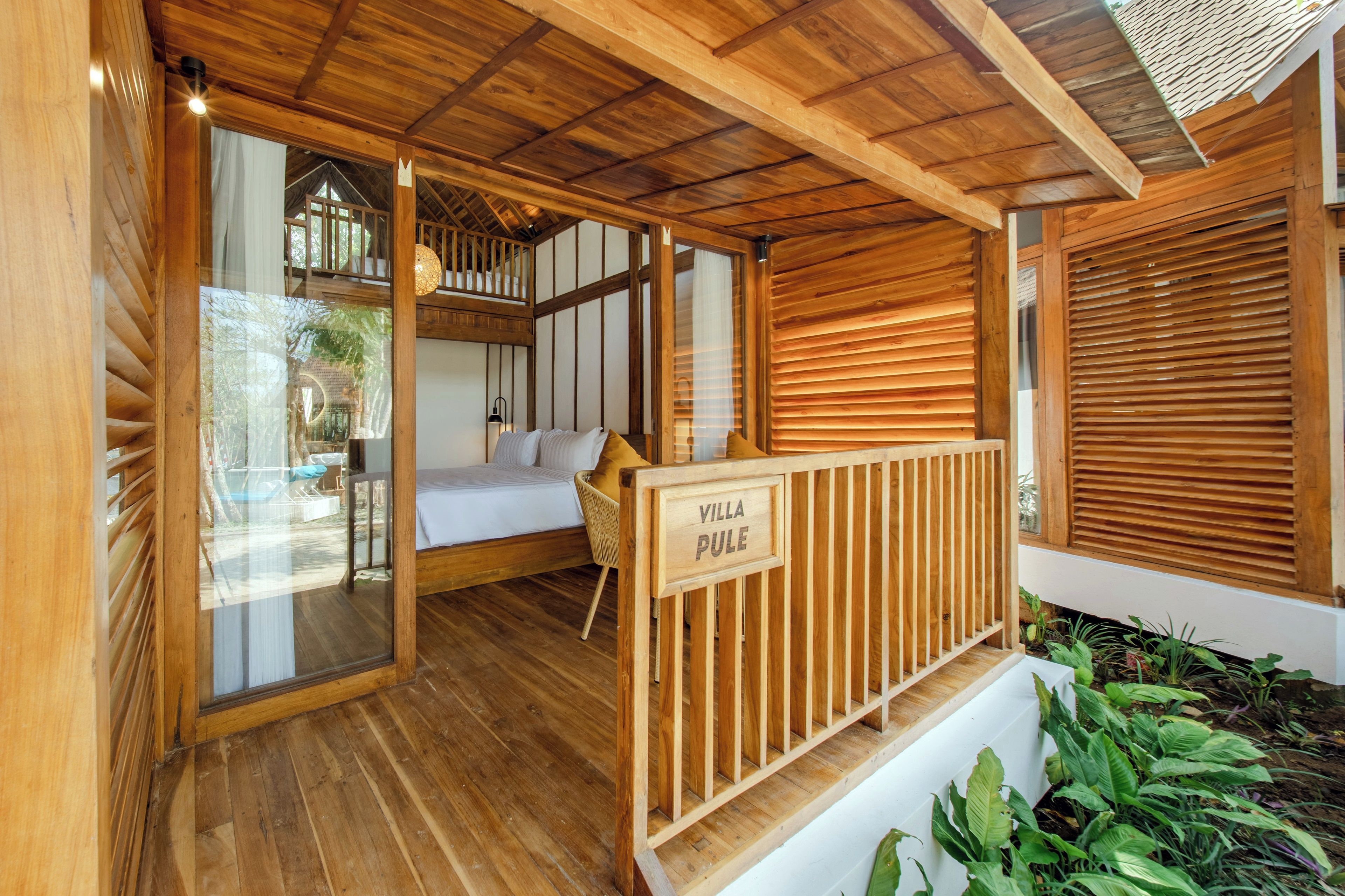Interior de una cabaña de madera con una cama, zona de estar y un balcón.