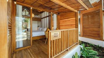 Interior de una cabaña de madera con una cama, zona de estar y un balcón.