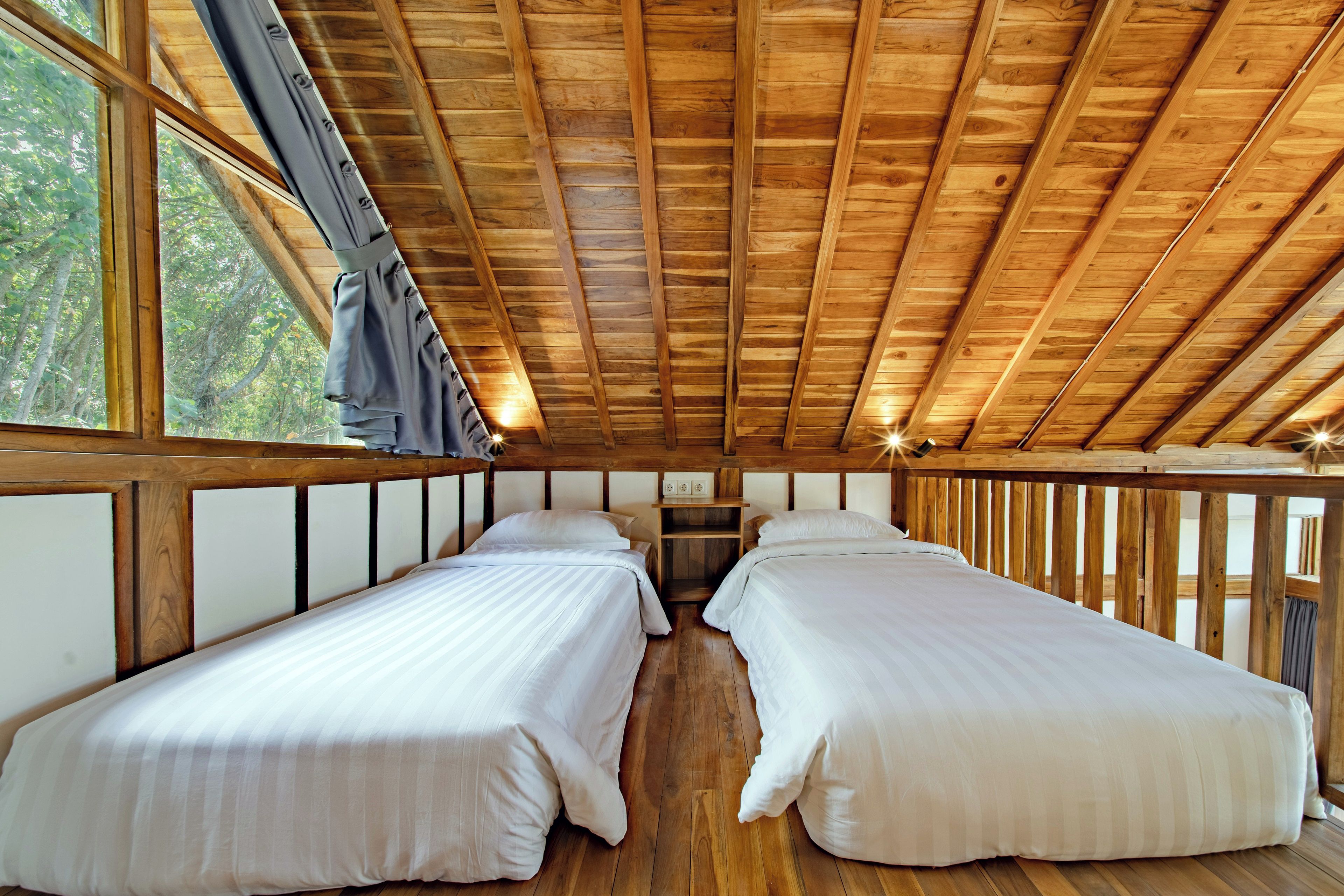 A cabin with two beds, wooden beams, and a window overlooking greenery.