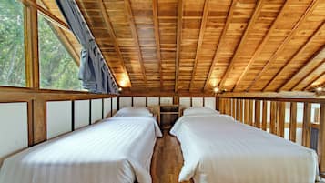 A cabin with two beds, wooden beams, and a window overlooking greenery.