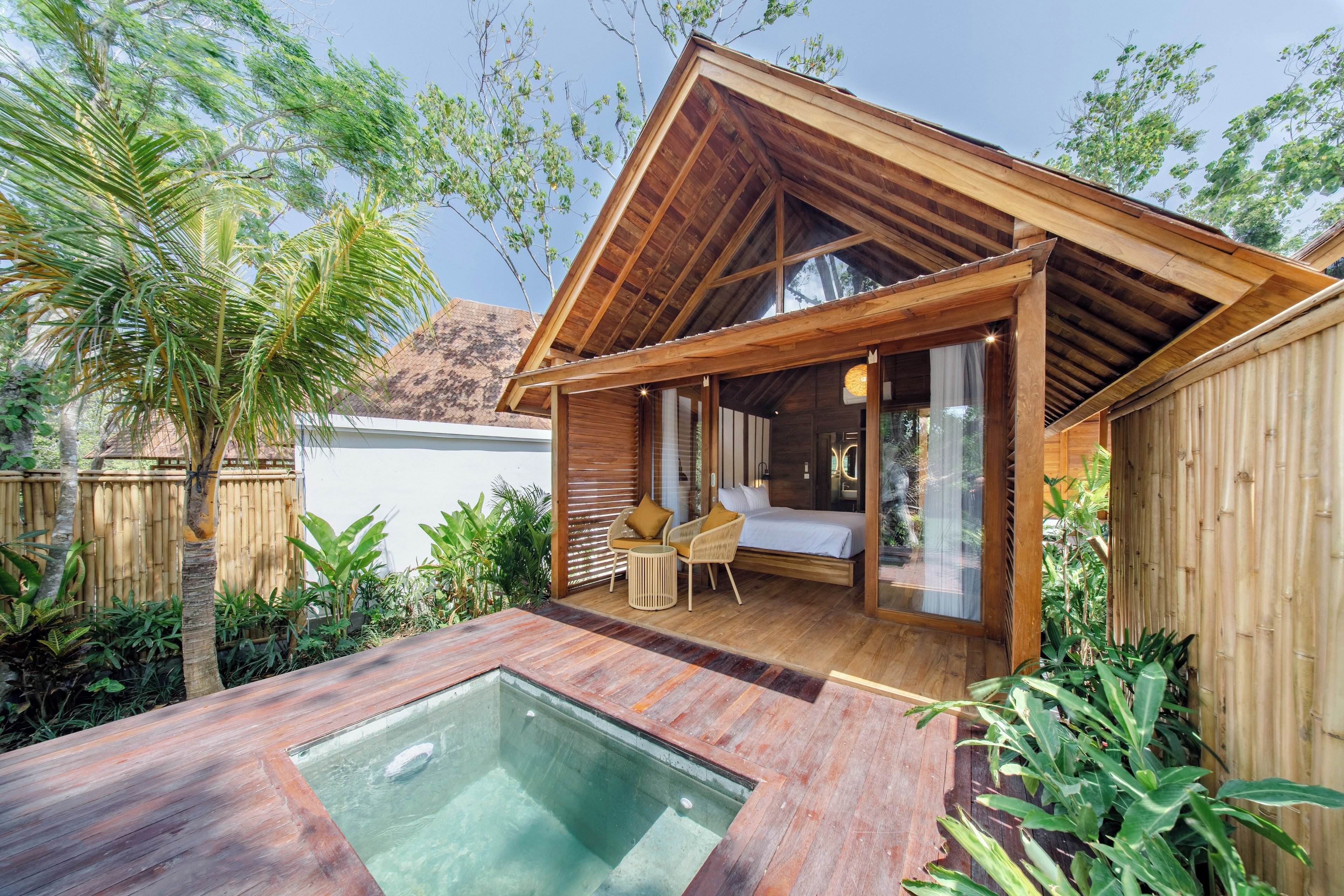 A wooden cabin with a glass-enclosed bedroom, a hot tub, and a patio area with plants.