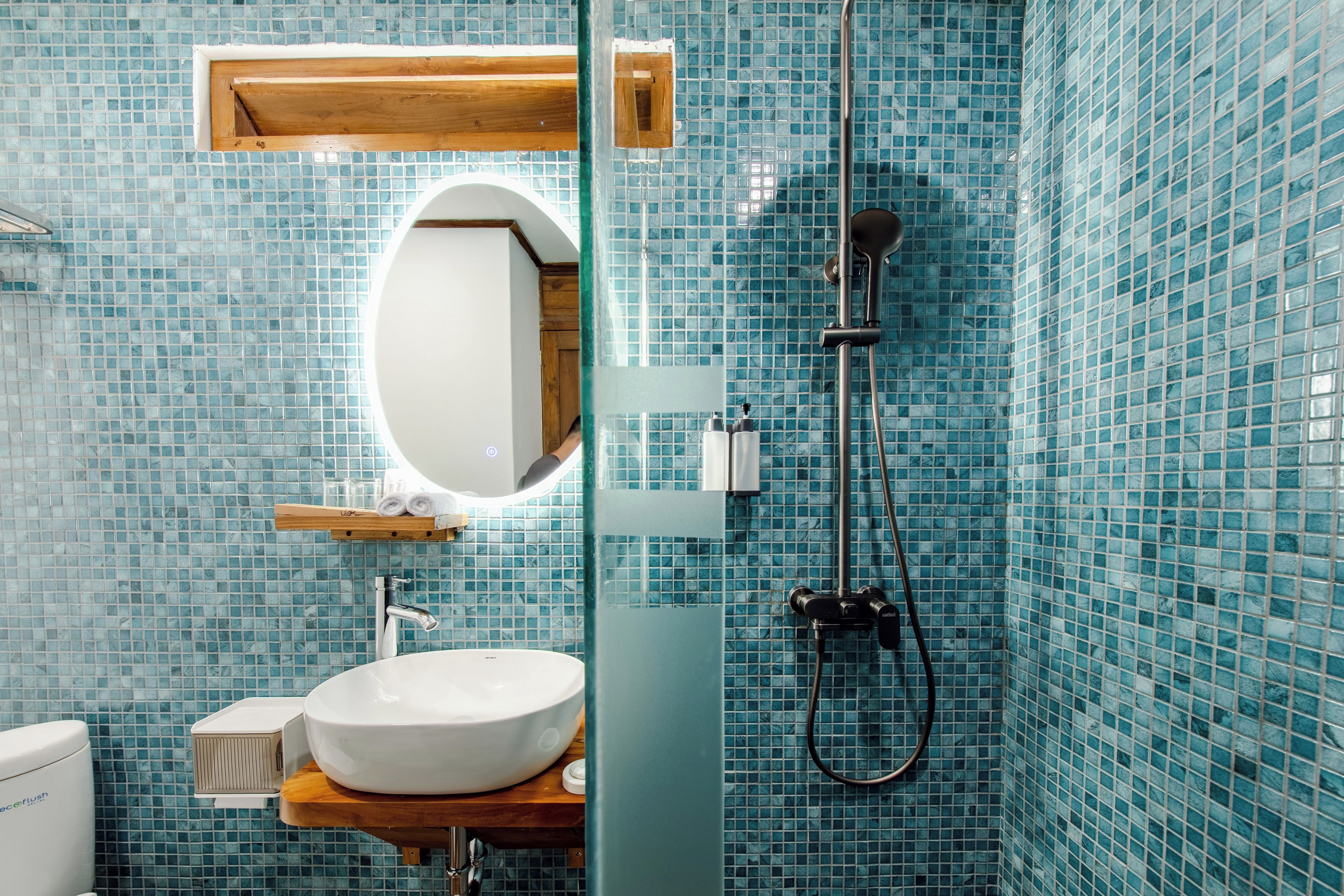 A bathroom with a white sink, a mirror, a shower head, and a tiled wall.