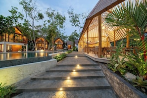 A resort with a swimming pool, wooden cabins, and a covered outdoor seating area. - Semara Gangga Beach Retreat (Tabanan)