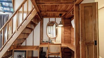 A wooden staircase leading to a loft bedroom with a desk, chair, and a small refrigerator.