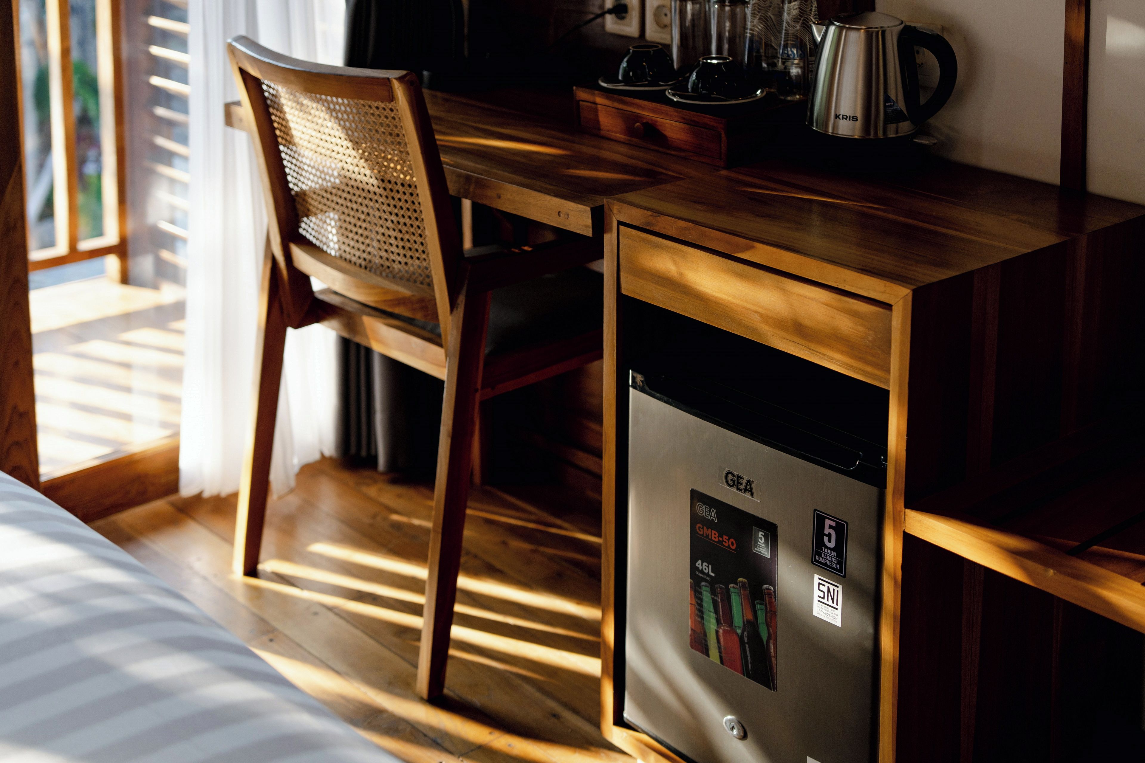 Un escritorio de madera con un refrigerador GEA, una silla y una tetera sobre la mesa.