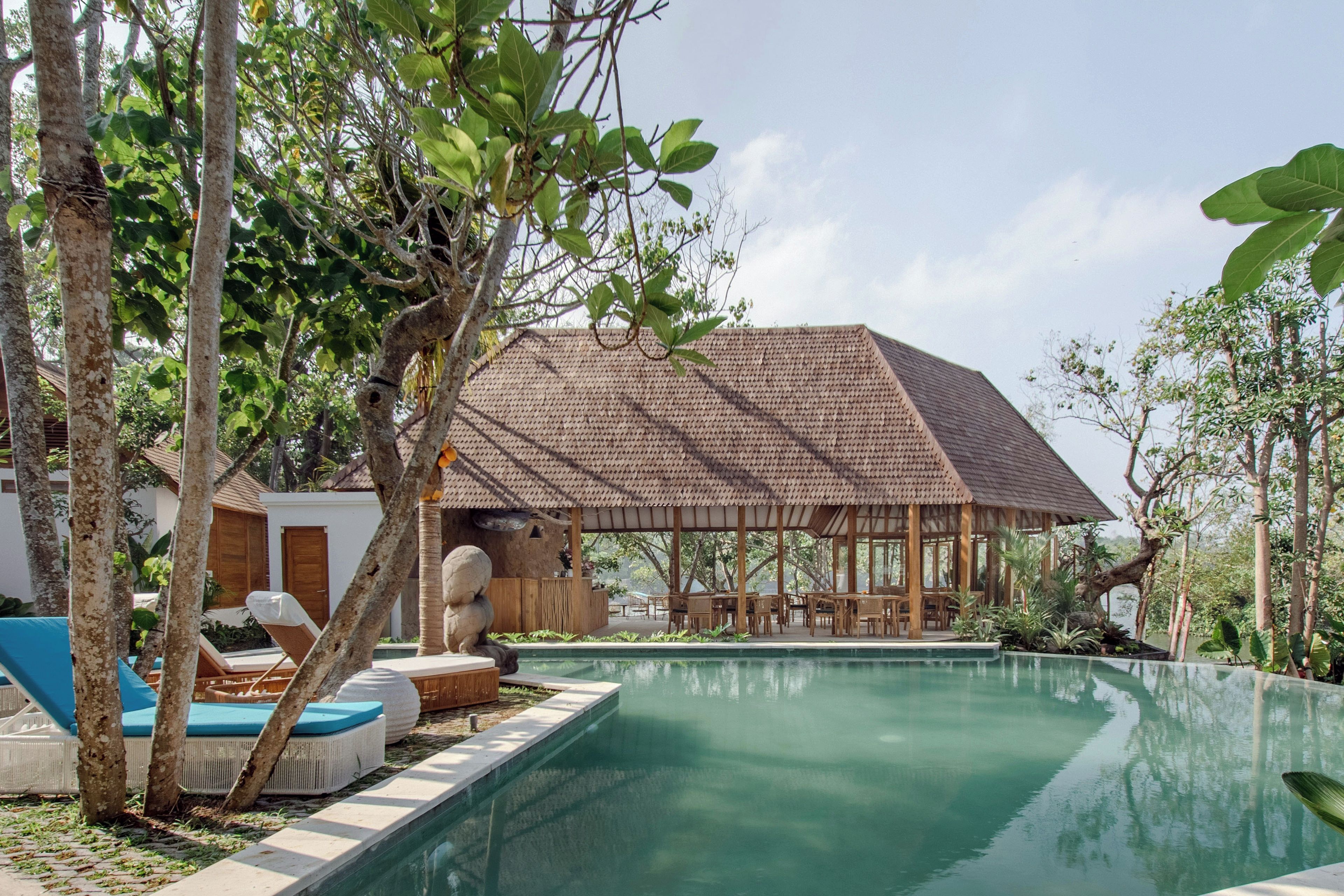 A pool area with lounge chairs, a covered seating area, and a building with a tiled roof.